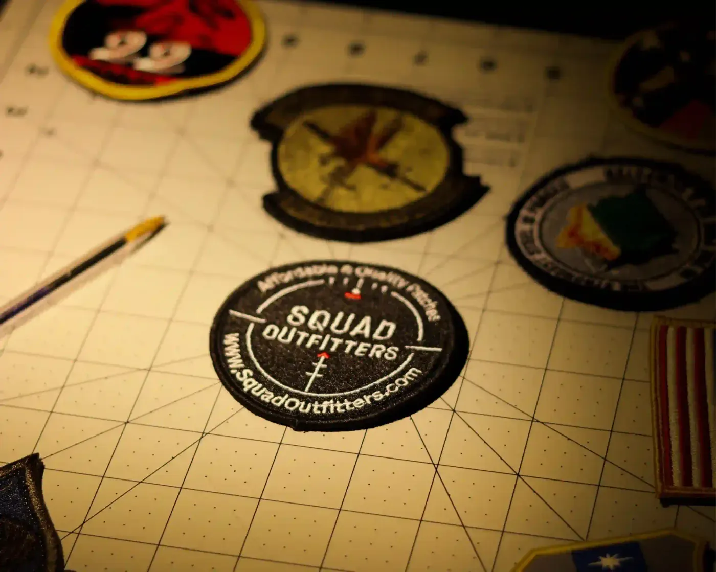 A Squad Outfitters embroidered patch on a cutting mat, surrounded by finished unit patches.