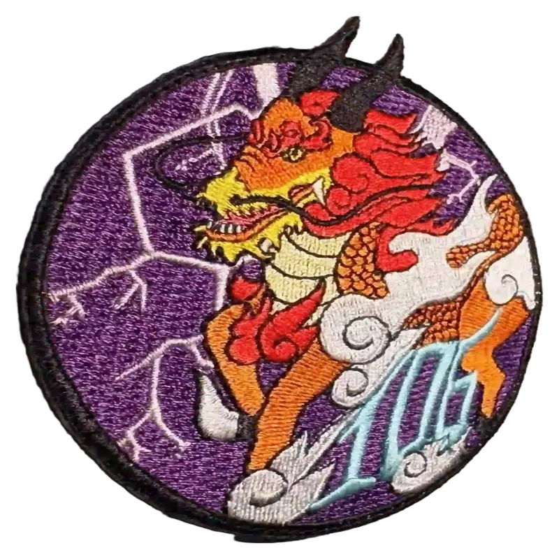 A custom embroidered patch showing a dragon design in red, orange and white thread on a purple twill field, bordered by a black merrowed edge.